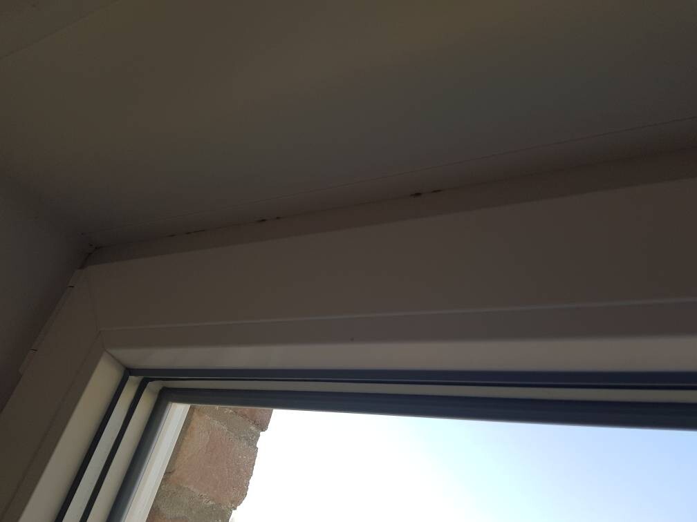 Fensterrahmen im Innenraum, Blick nach außen auf Ziegelwand und blauen Himmel.