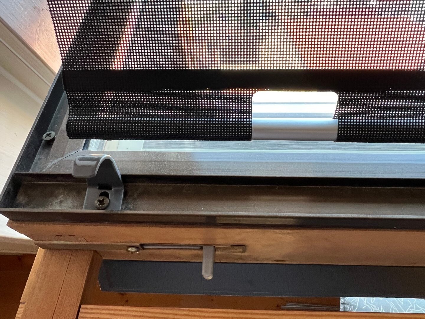 Schwarzes Netzrollo am Fenster; seitlich montierte Halterung, Metallrohr sichtbar, Innenrahmen.