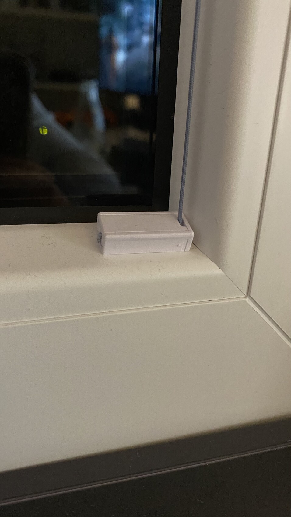 Kleine weiße rechteckige Box auf Fensterbank neben Fensterrahmen; blaues Kabel verläuft daneben.