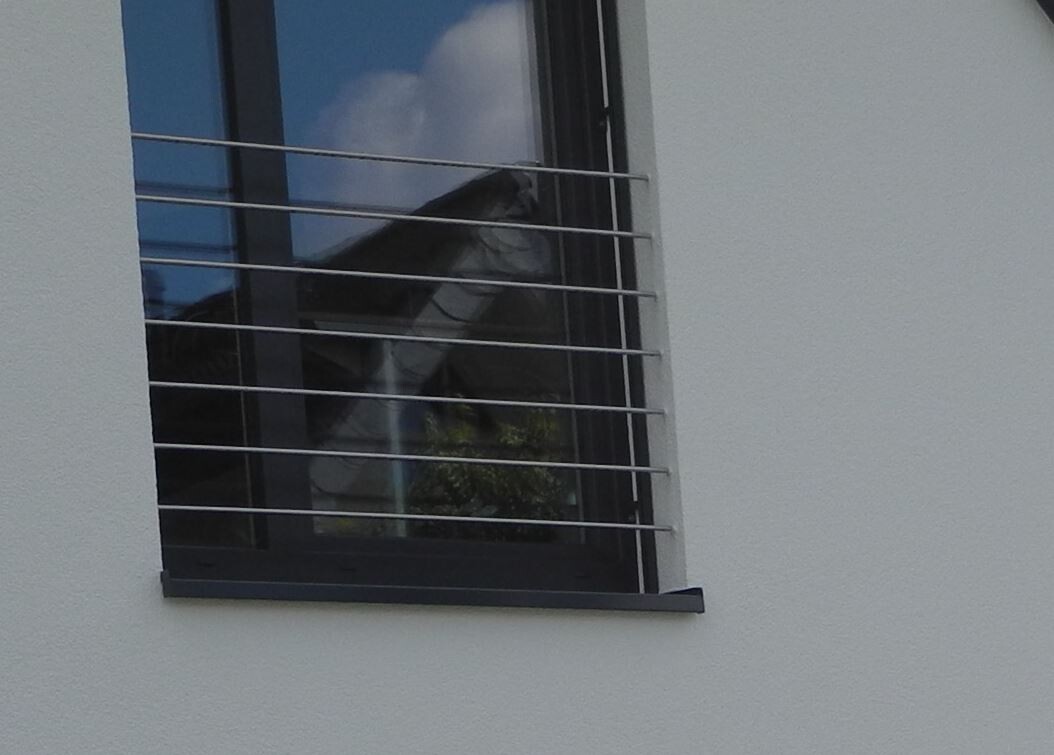Fenster eines weißen Gebäudes mit horizontalen Metallstäben als Gitter; Reflektion von Himmel.