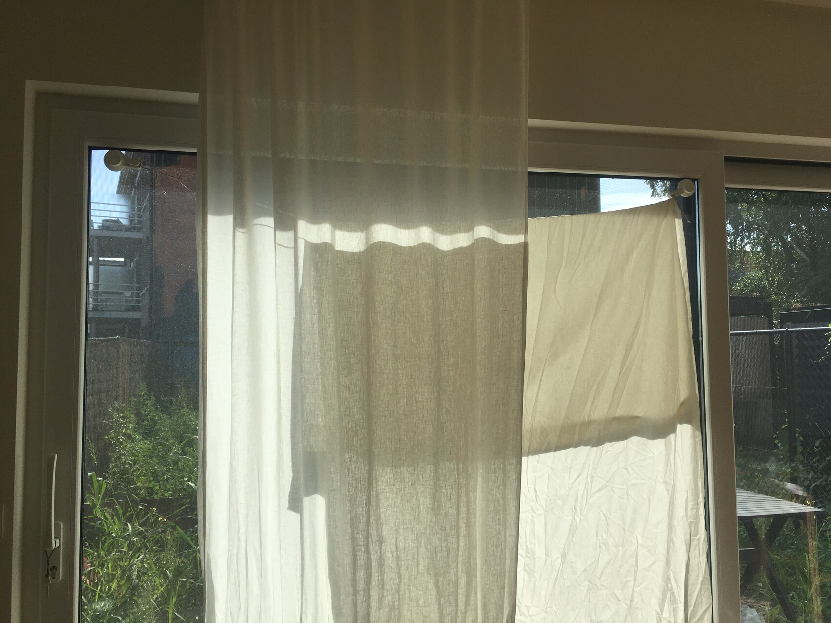Innenraum mit Glasschiebetür; durchsichtiger Vorhang, draußen hängt weißes Tuch auf der Leine.
