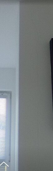 Innenraum: linke Seite mit Fenster und Rollläden, weiße Wand; rechts beige Wand mit dunklem Rahmen.