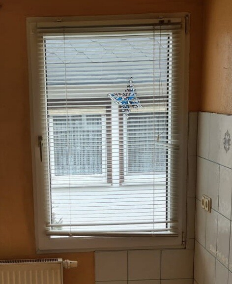 Fenster mit horizontalen Jalousien; ein blauer Stern als Dekoration hängt an der Scheibe.