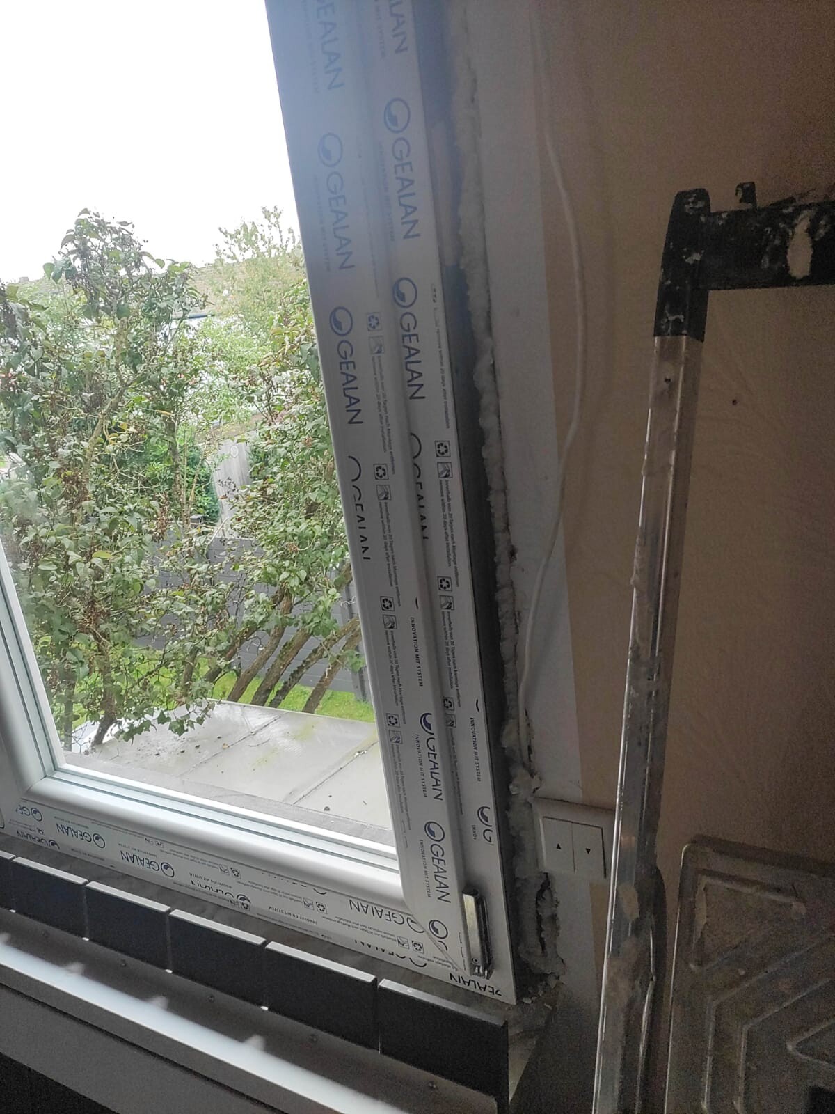Innenraum: Fenstermontage mit Schutzverpackung am Rahmen, Blick nach außen auf Bäume