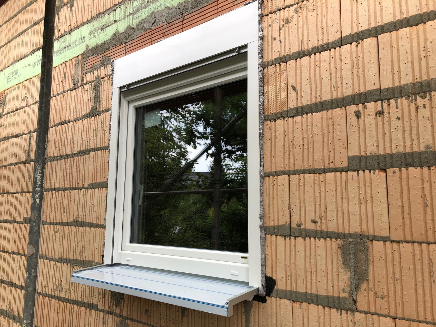 Weißer Fensterrahmen vor roter Ziegelwand; Bauarbeiten, Baumreflektion im Glas.