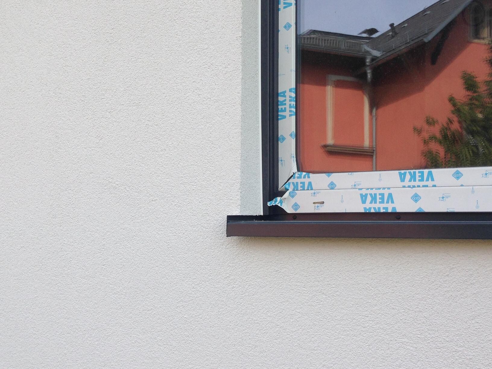 Außenwand mit neu installiertem Fensterrahmen und Schutzfolie, rotes Nachbarhaus im Hintergrund
