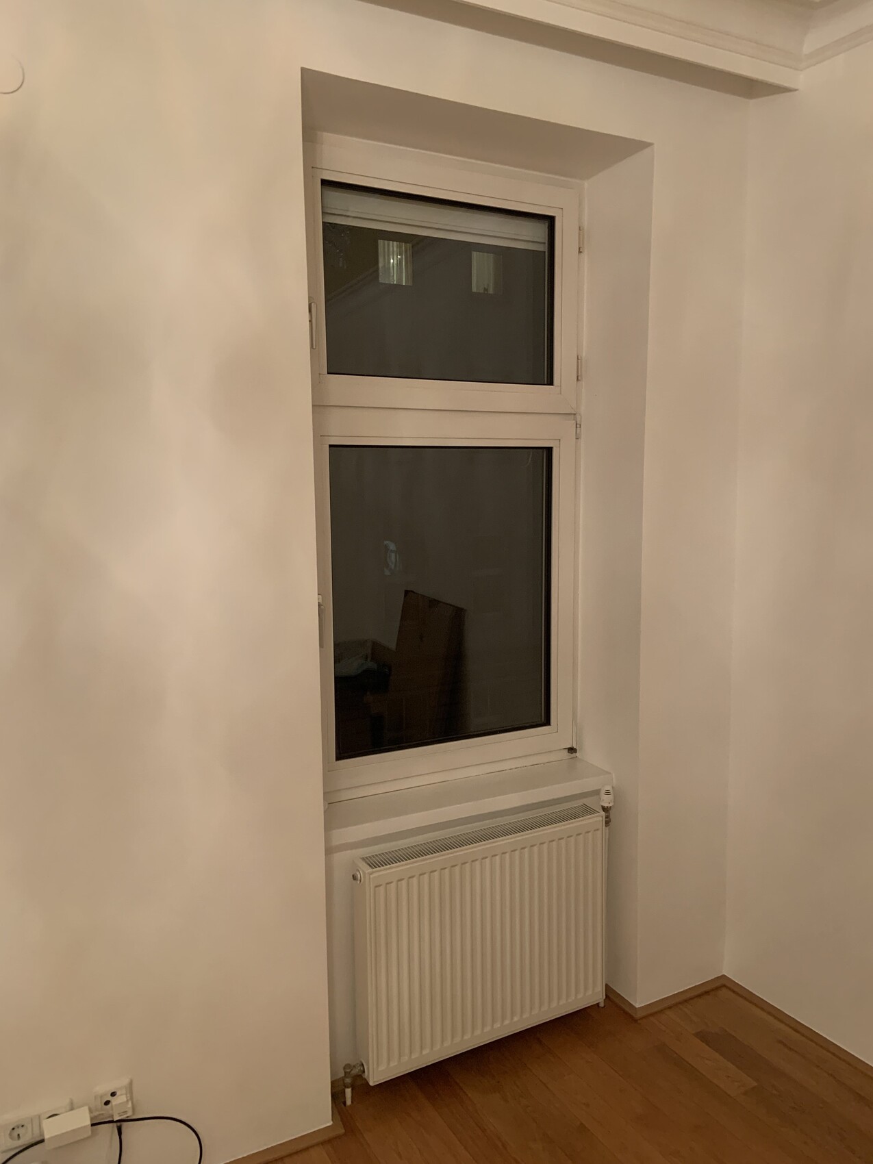 Innenraumecke mit Fenster über dem Heizkörper; weiße Wände und Holzboden.