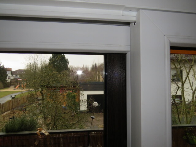 Fensterrahmen mit Aussicht auf Garten, Bäume und Nachbarhäuser