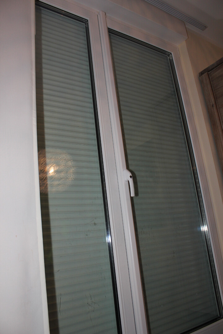 Weißer Fensterrahmen mit Griff, geschlossene Glasscheiben und Innenrollos im Innenraum