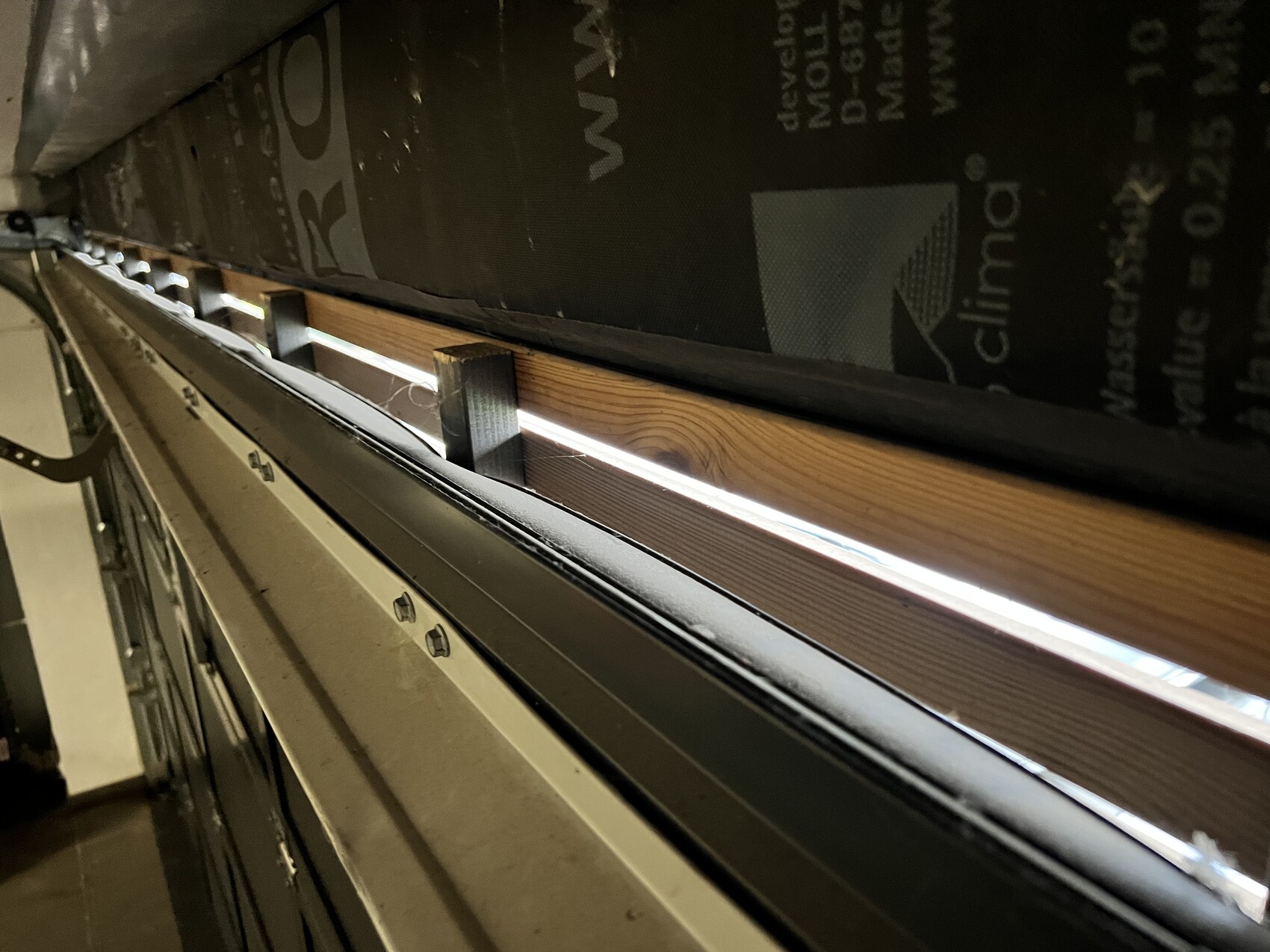 Nahaufnahme eines Rollladenfensters von unten: Holzrahmen, Metallführung und Lichtstreifen durch Spalt