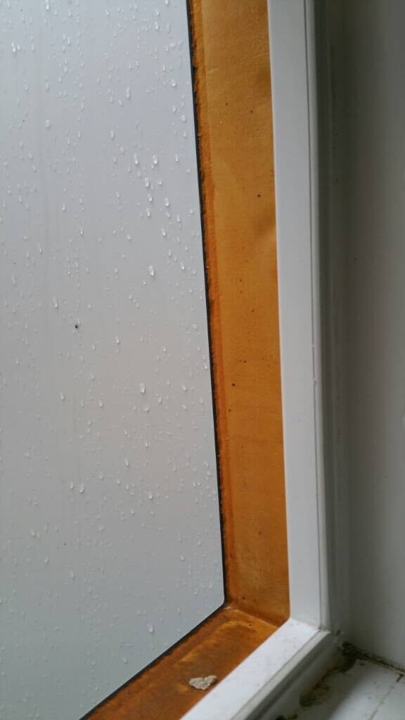 Nahaufnahme eines Fensters mit Regentropfen auf Glas und orangefarbener Dichtungsleiste am Rahmen