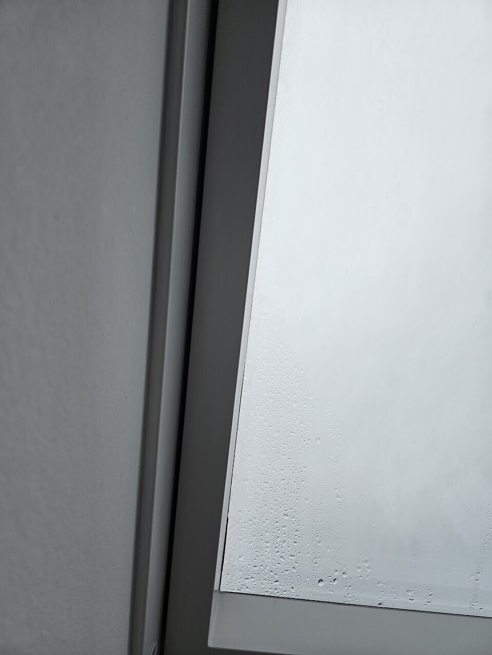 Nahaufnahme eines Fensterrahmens mit weißem Fenster und Wassertröpfchen am Glas.