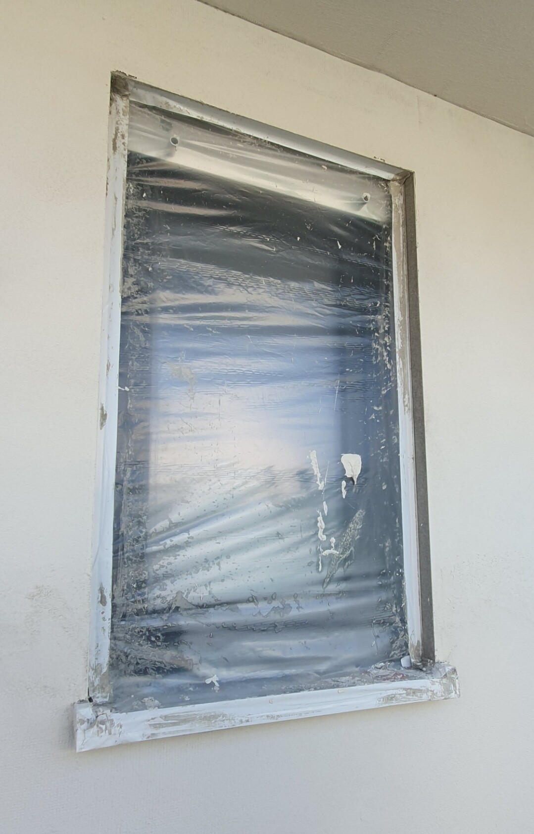 Fensterrahmen mit transparenter Schutzfolie an heller Wand; Folie verschmutzt und beschädigt.