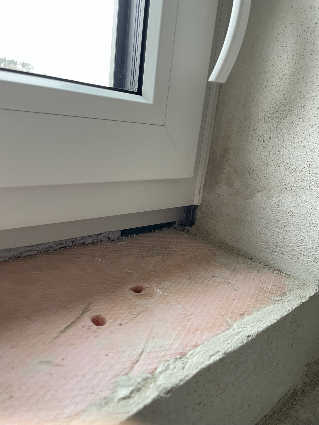 Fensterrahmen im Rohbau mit Dämmplatten und rohem Putz an der Fensternische