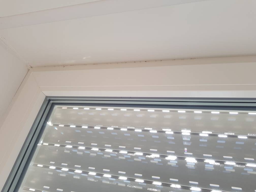 Innenansicht eines Fensters mit weißem Rahmen; horizontale Lichtreflexe auf der Glasscheibe.
