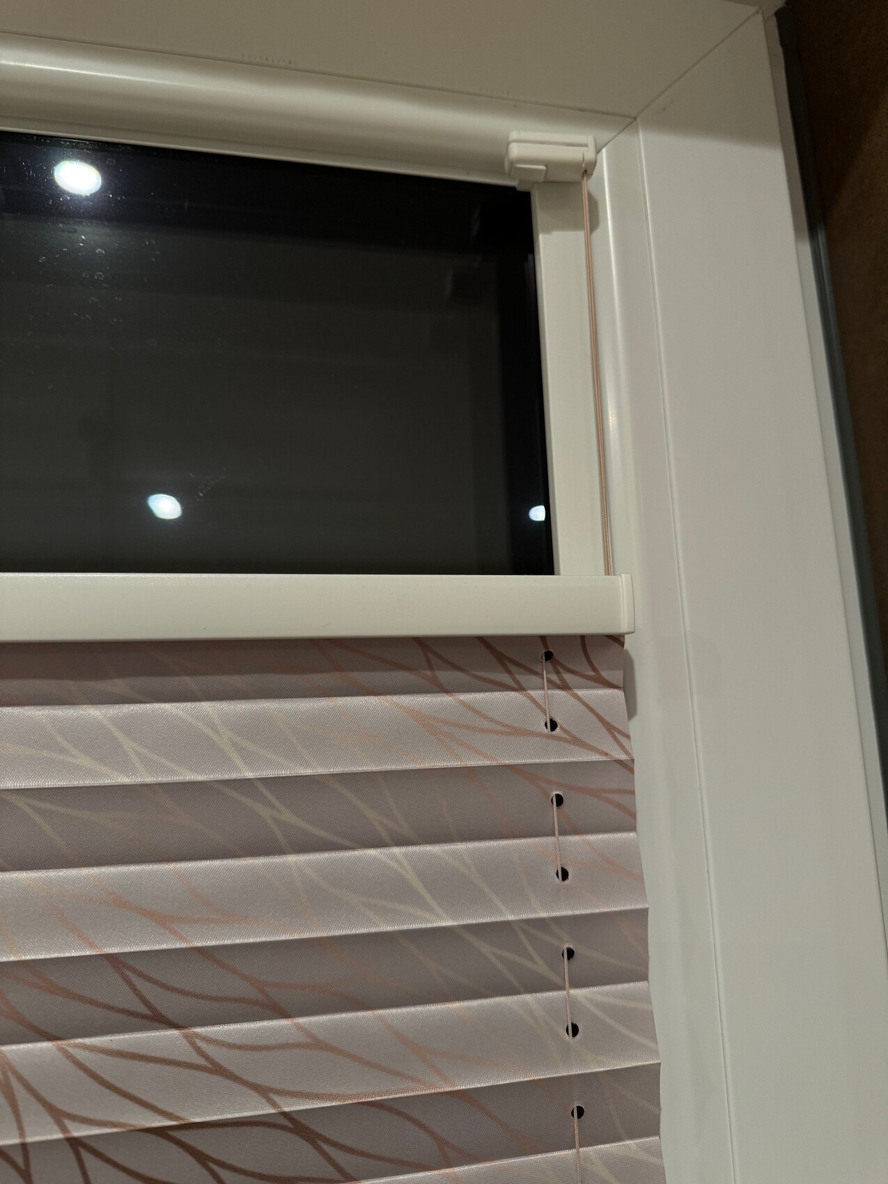 Weißer Fensterrahmen mit sichtbaren Zugkordeln; helle Stoffjalousie mit Wellenmuster.