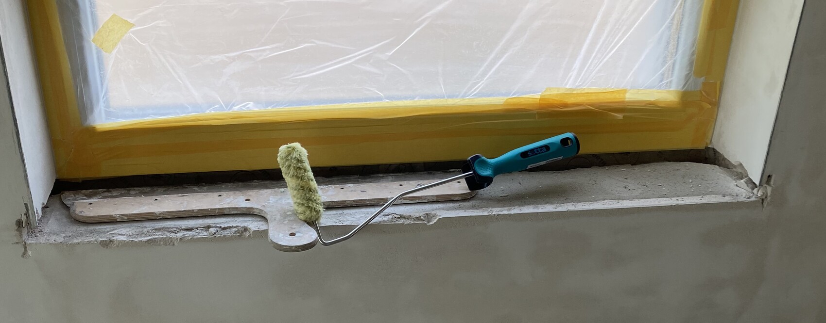 Pinselroller liegt auf Fensterbank während Innenrenovierung, Fensterrahmen mit Abdeckung.
