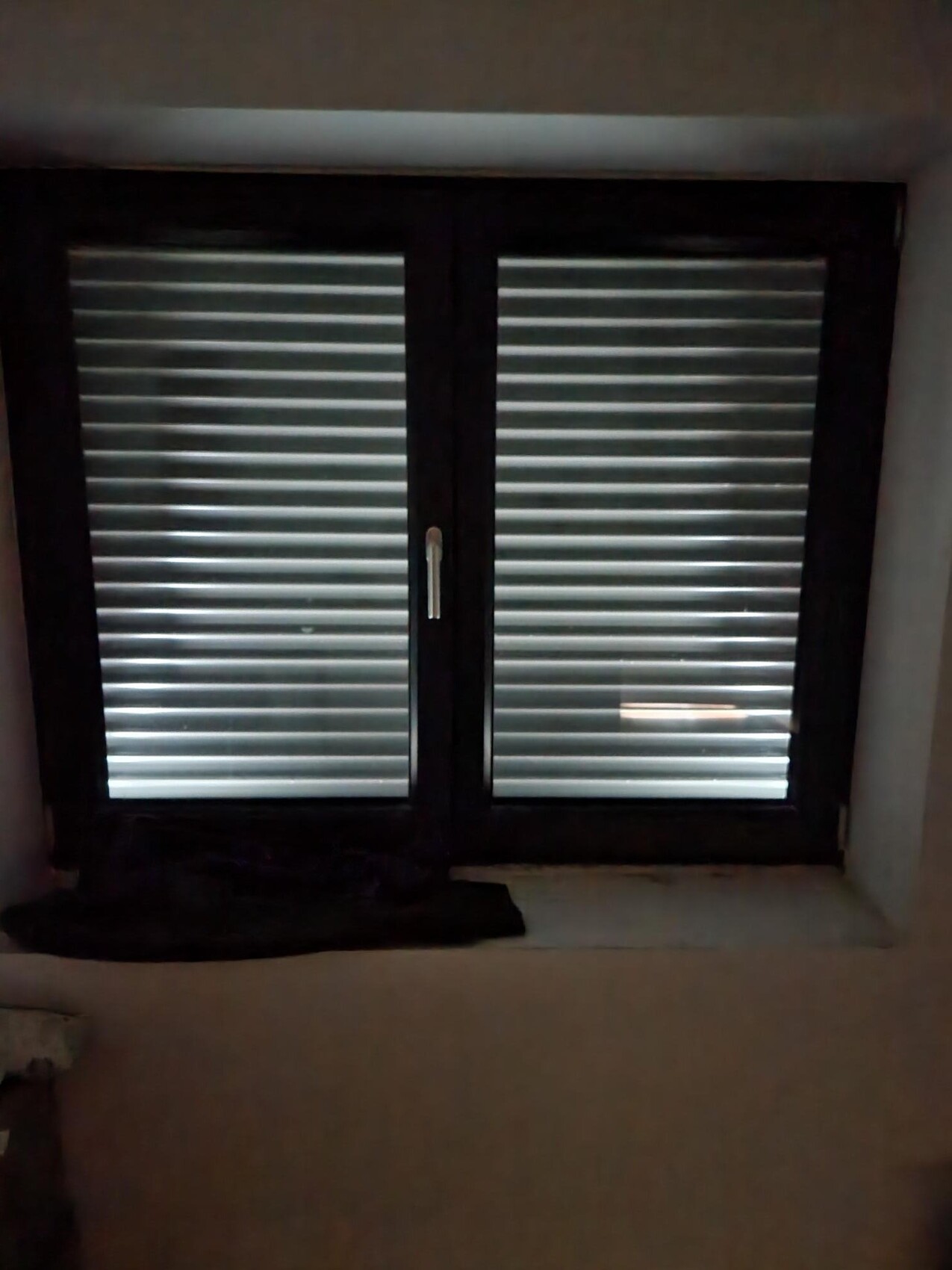 Zweiflügeliges Fenster mit geschlossenen horizontalen Rollläden im dunklen Raum.
