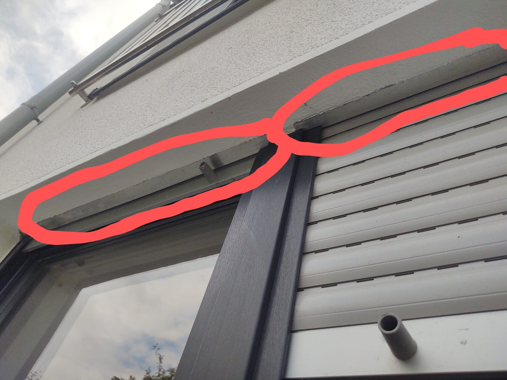 Außenfenster mit Rollladen; rote Markierung um einen Putzriss über dem Rahmen.