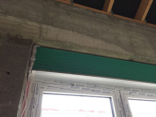 Fenster mit grünem Rollladen in einer Baustelle, Rohbau sichtbar.