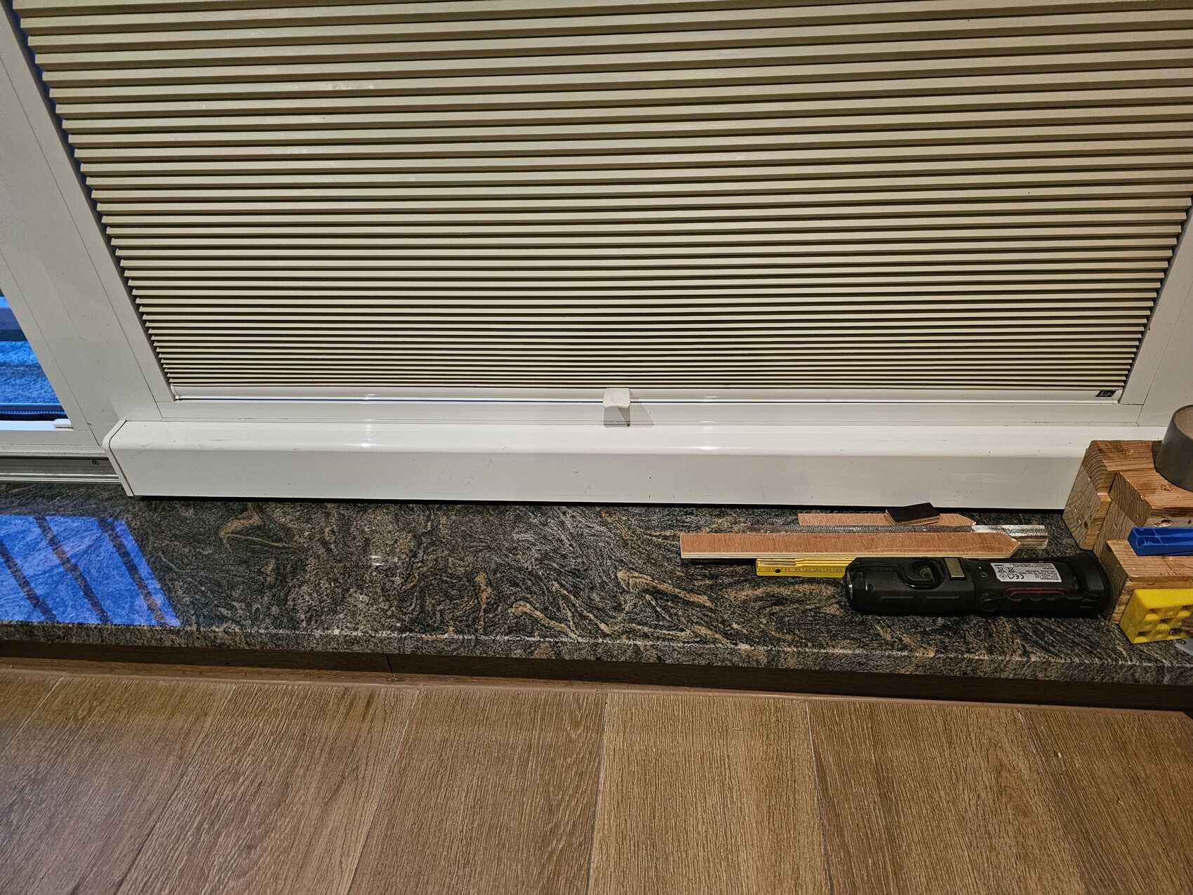 Fenster mit geschlossenen Jalousien, Steinfensterbank; Akku-Bohrmaschine, Schleifpapier, Holzklötze.
