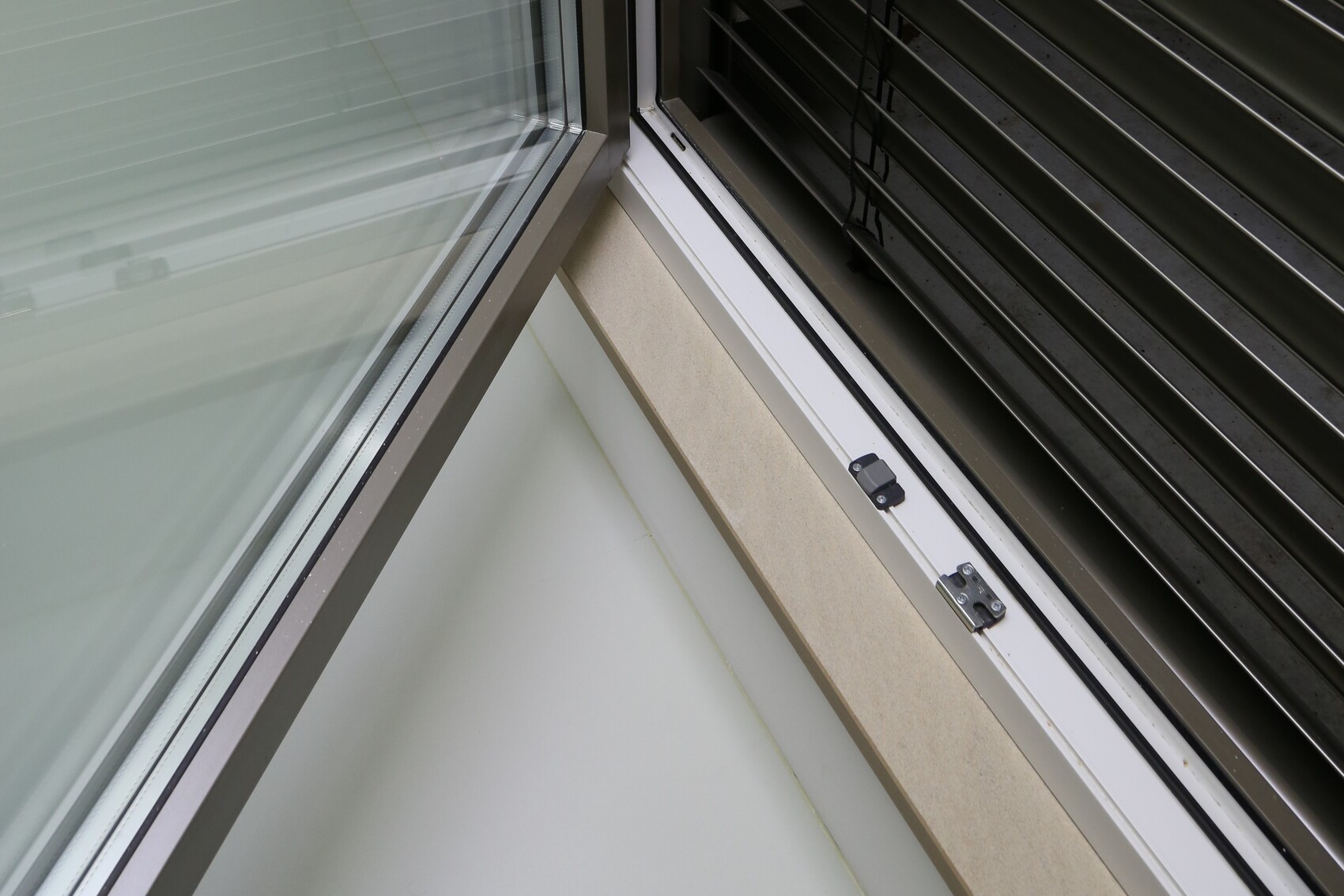 Eckfenster mit geschlossener Jalousie, Glasrahmen und heller Fensterbank.