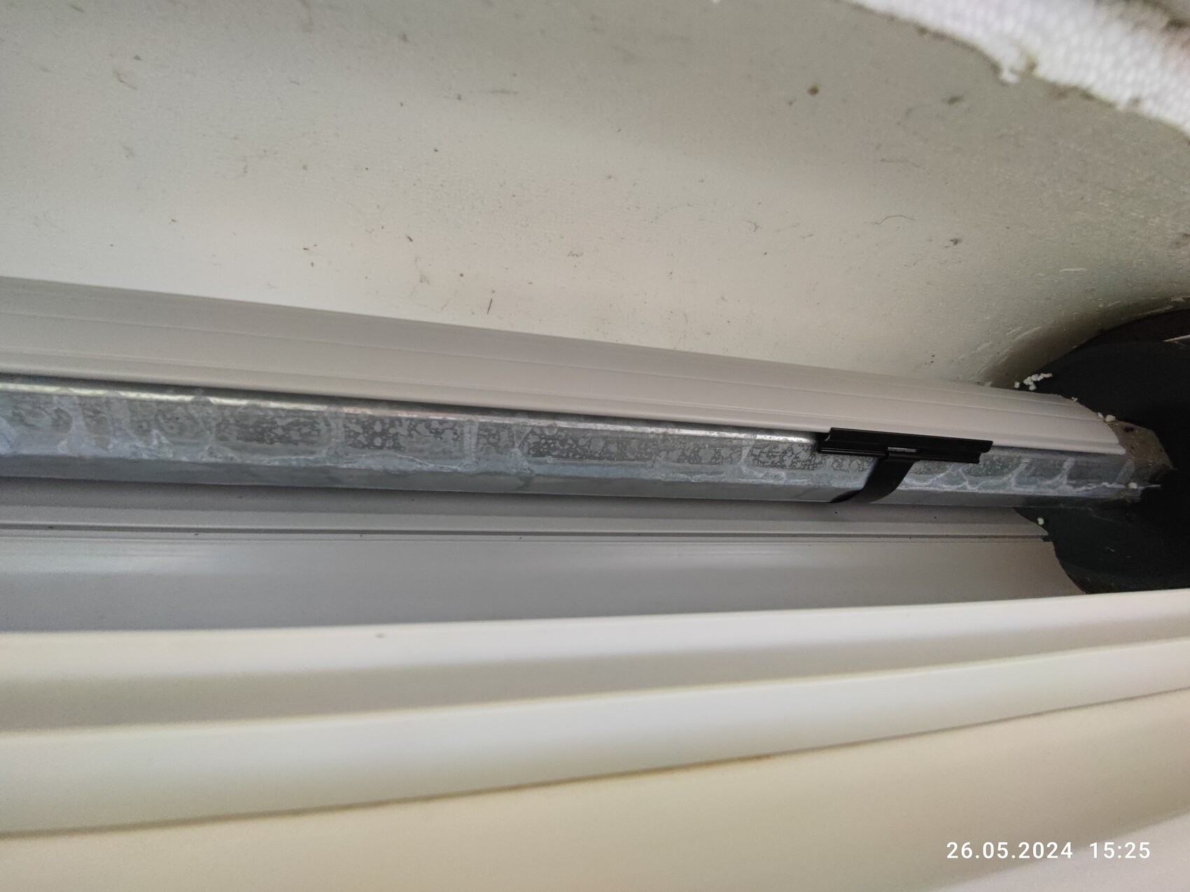 Nahaufnahme einer silbernen Metall-Schiene mit schwarzer Halterung an einer Tür- bzw. Fensterführung.