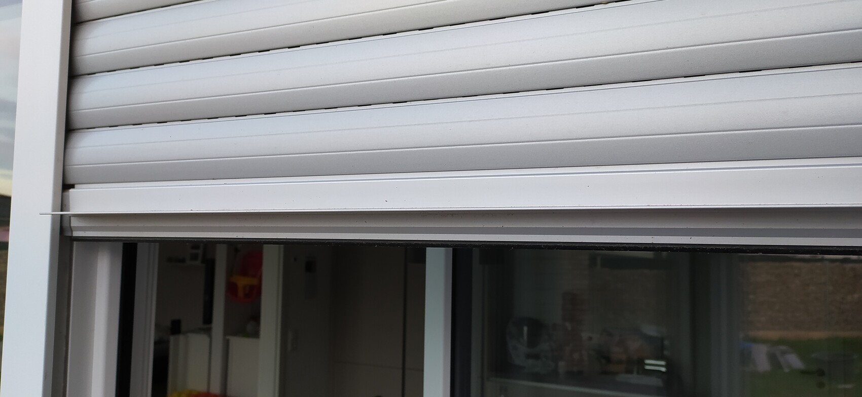 Weißer horizontaler Rollladen über Fenster; Innenraum mit Möbeln sichtbar.