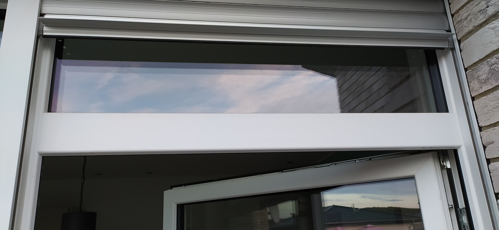 Außenansicht: weißer Fenster- und Türrahmen, oberer Rollladen, Himmel im Glas gespiegelt