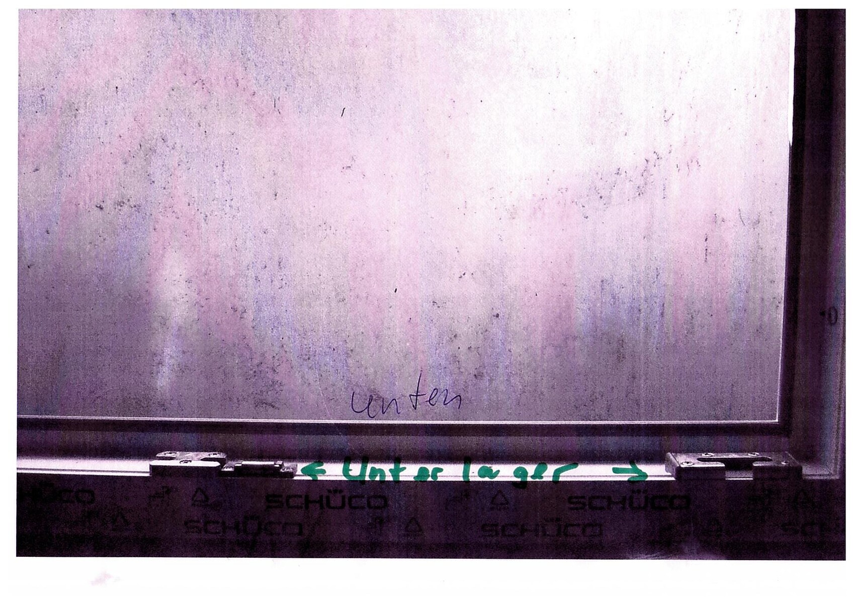 Verstaubtes, pink-getöntes Fensterglas mit Schüco-Rahmen; unten handschriftlich "unten".