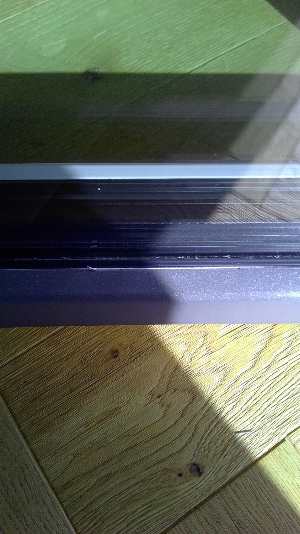 Nahaufnahme eines Fensterrahmens mit Glas und Holzfussboden im Vordergrund