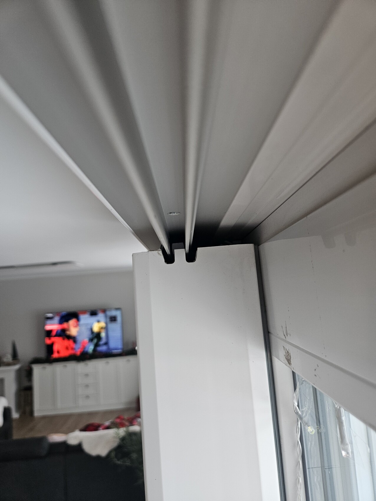 Weisser Fensterrahmen mit Fuehrungsschiene im Innenraum, Blick ins Wohnzimmer mit Fernseher.