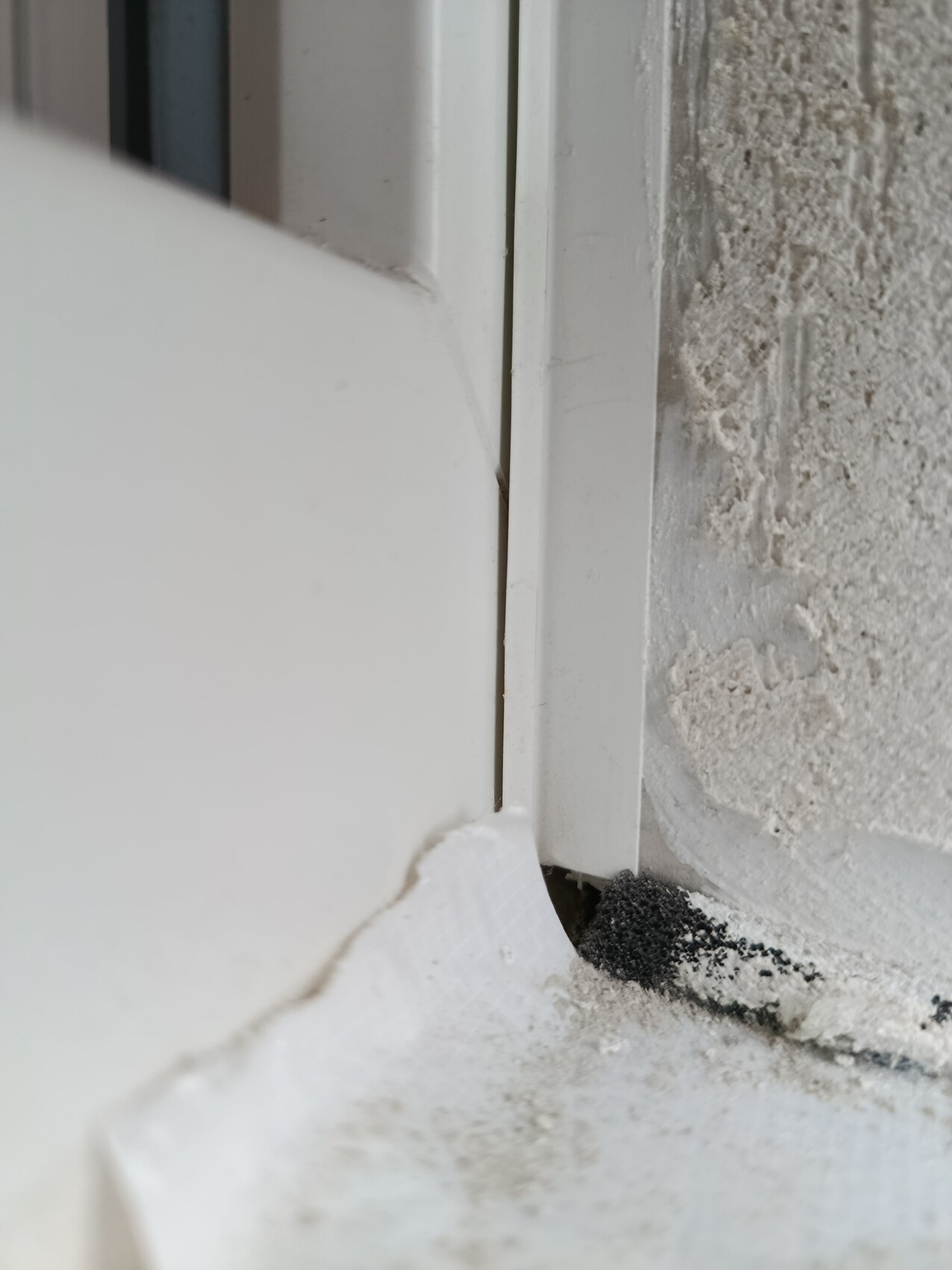 Nahaufnahme eines weißen Fensterrahmens an unfertiger Wand mit Staub und Spachtelmasse