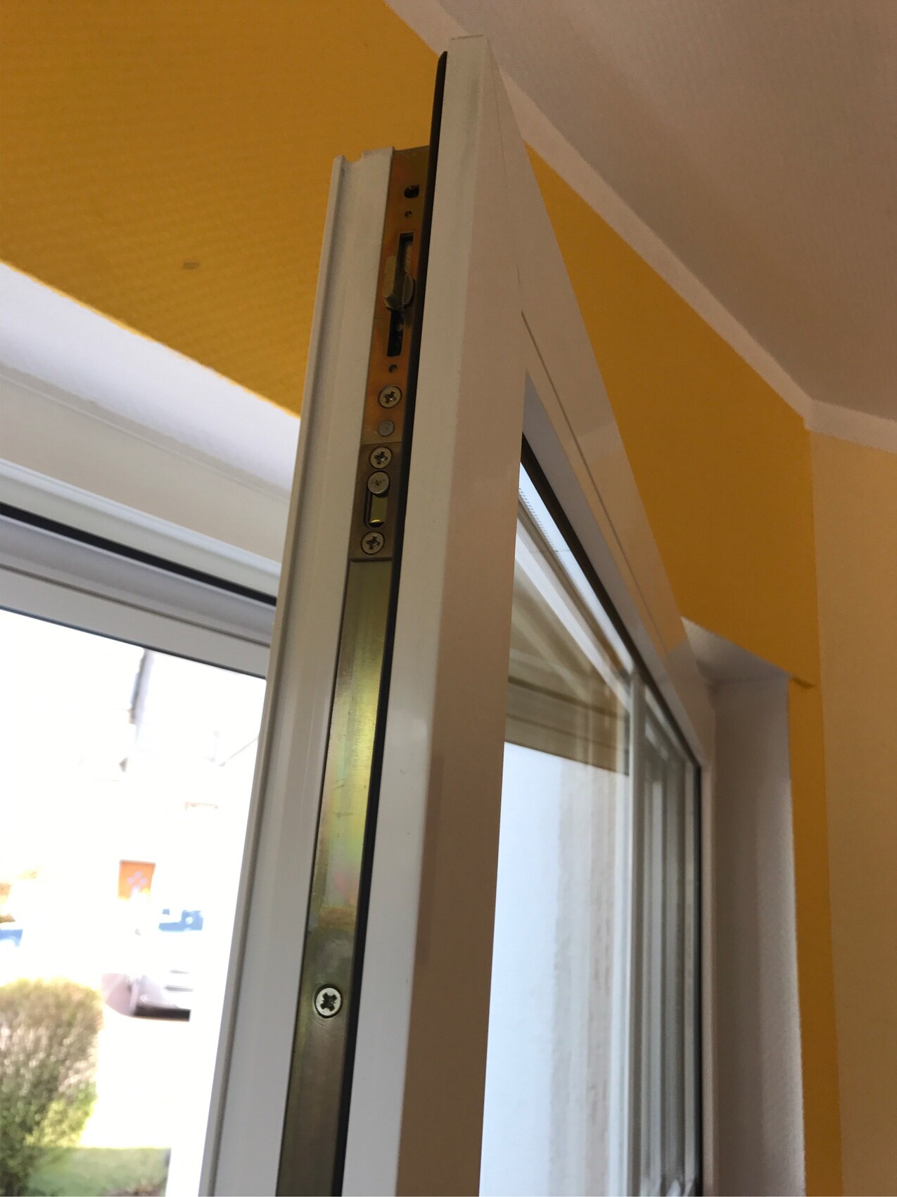 Nahaufnahme eines weißen Türrahmens mit Metallbeschlag und Scharnier, gelbe Wand dahinter.