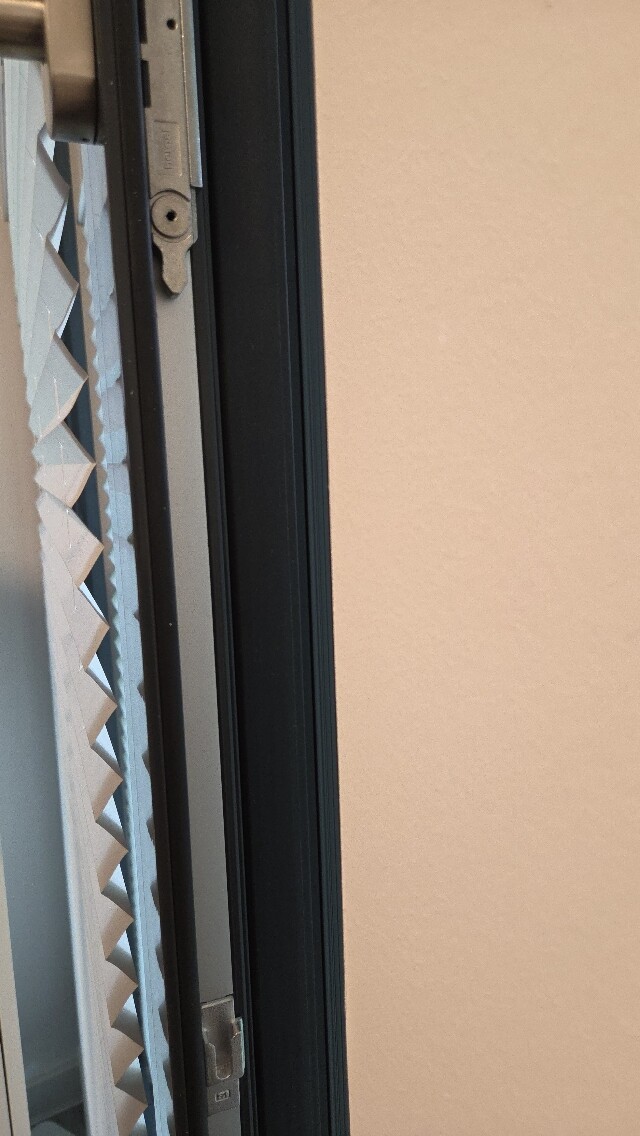 Nahaufnahme eines Fensterrahmens mit Lamellenjalousie am Rand und Wand dahinter