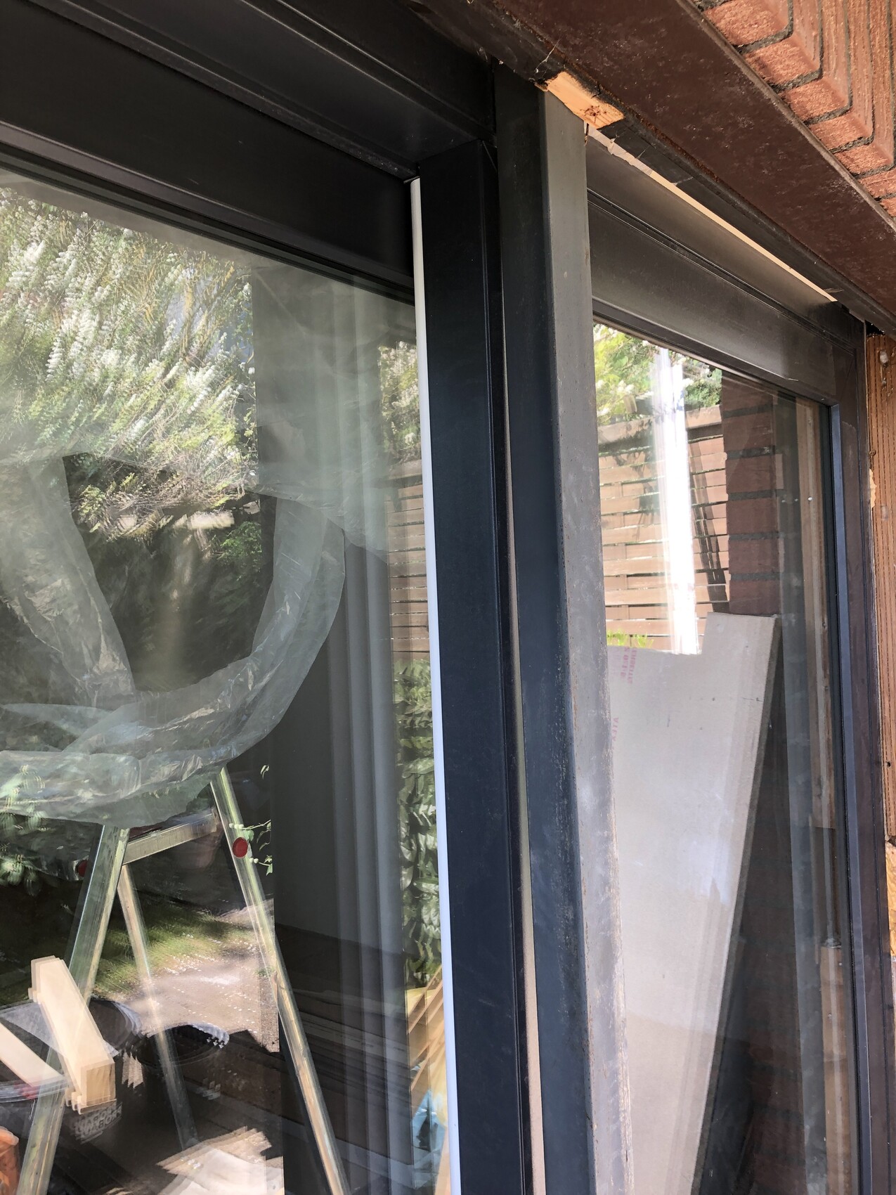 Große Glas-Schiebetür mit schwarzem Rahmen, Baustellenutensilien, Leiter und Plastikfolie davor.