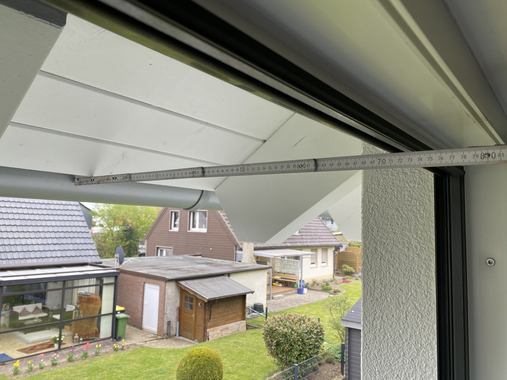 Blick durch geöffnete Balkontür mit Maßband über dem Rahmen auf Garten und Nachbarhäuser.