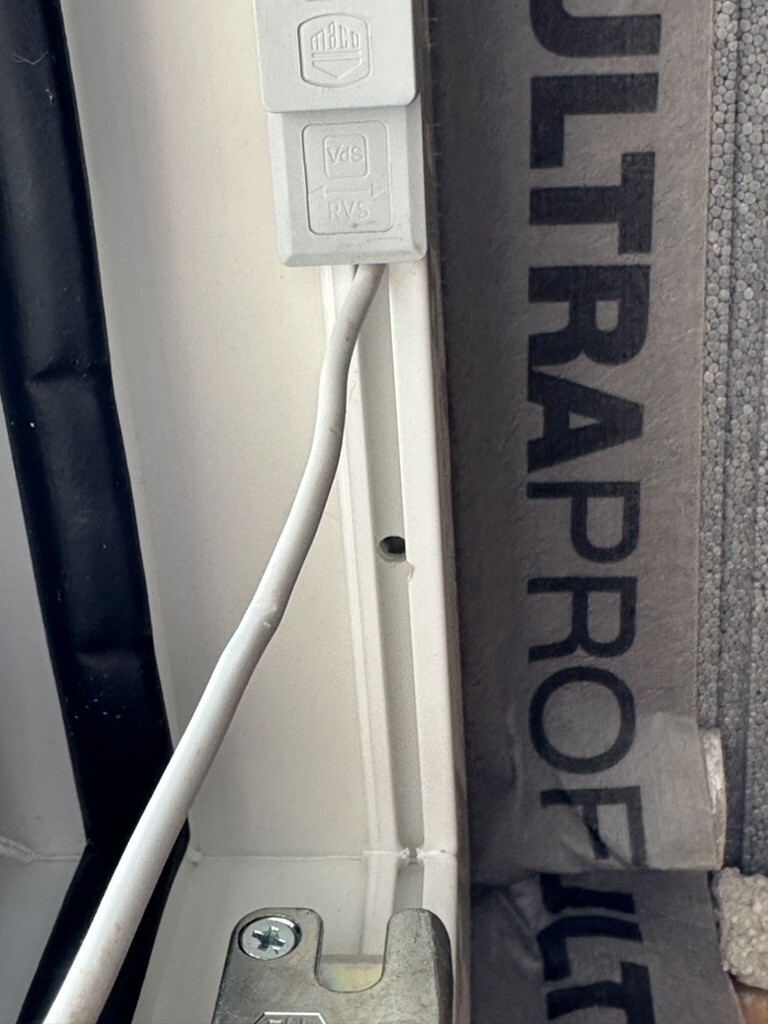 Türrahmen mit weißem Kabel und zwei grauen Klemmblöcken am Rahmen.