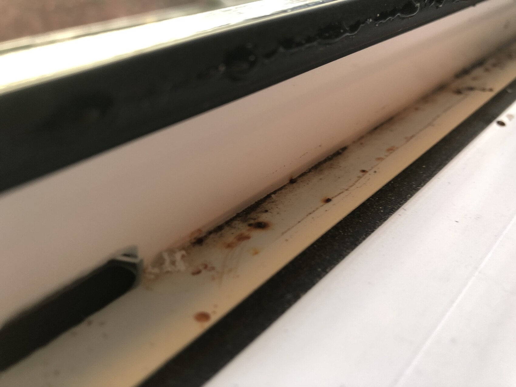 Nahaufnahme eines verschmutzten Fensterrahmens mit Rostflecken entlang der Schiene