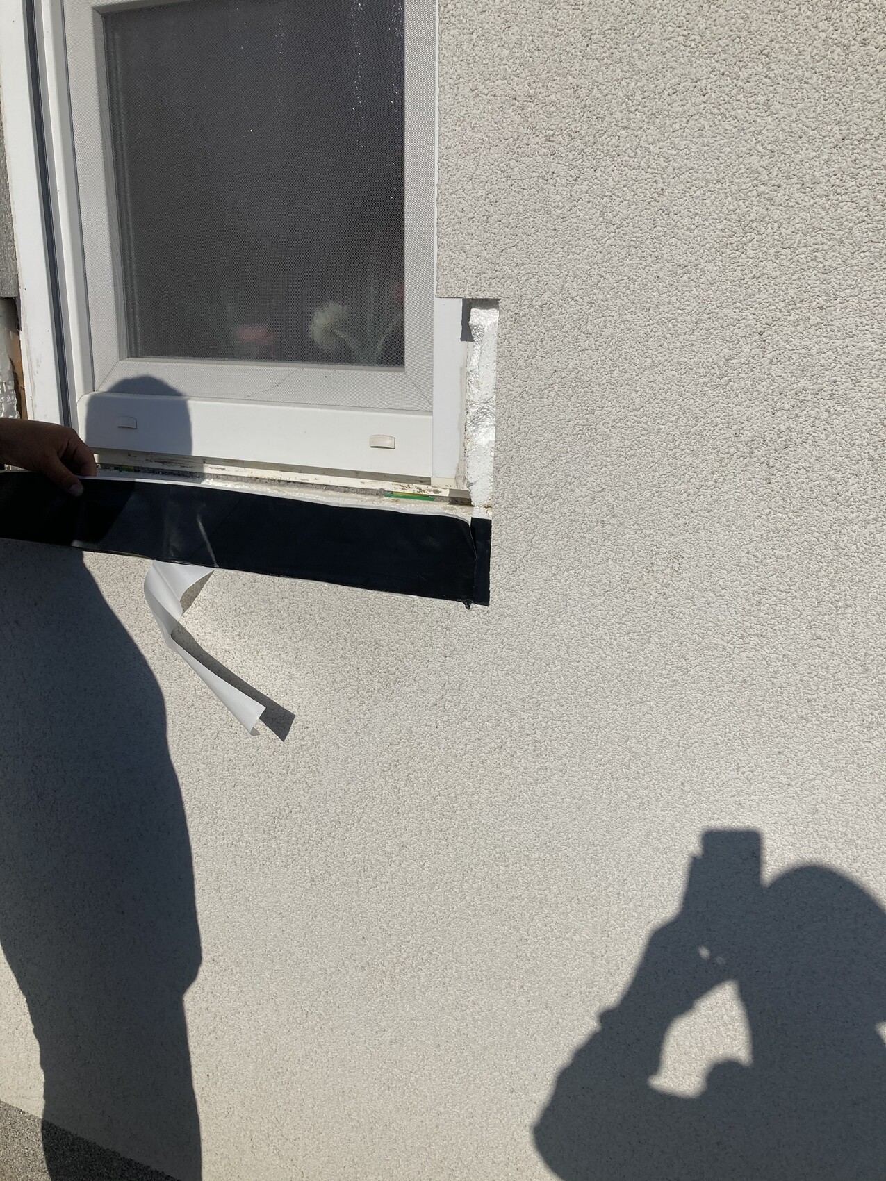 Außenwand mit kleinem Fenster; Hand hält schwarzes Klebeband am Rand.