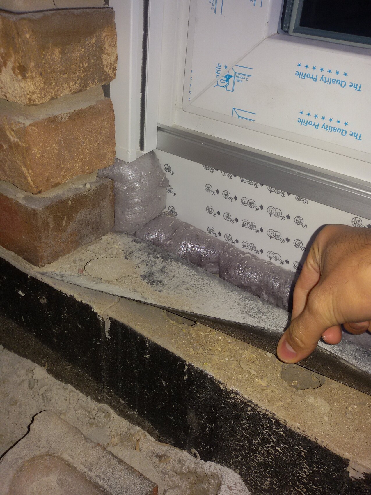Fensterlaibung: Ziegelwand, Dichtmasse, Isoliermaterial; Hand legt Kante an.