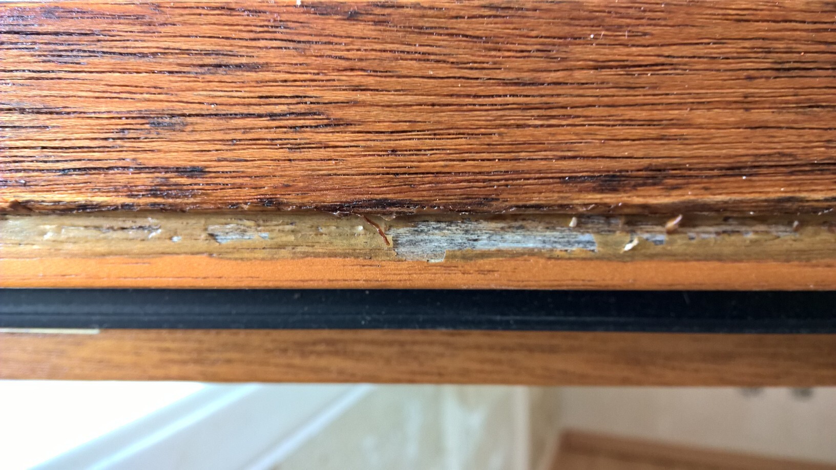Abgenutzte Fensterbank aus Holz mit Lackabplatzungen und Feuchtigkeitsschäden.