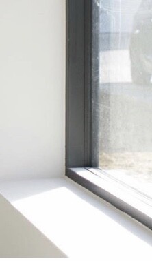 Weisses Fensterbrett mit dunklem Fensterrahmen und Sonnenlicht auf der Innenwand