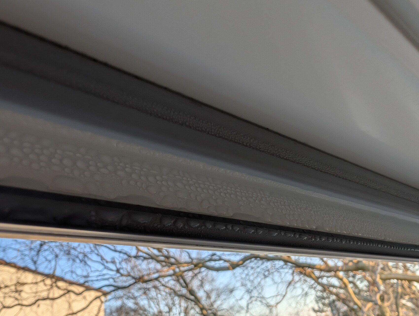 Nahaufnahme einer Fensterdichtung mit Wassertropfen, Außenlandschaft im Hintergrund