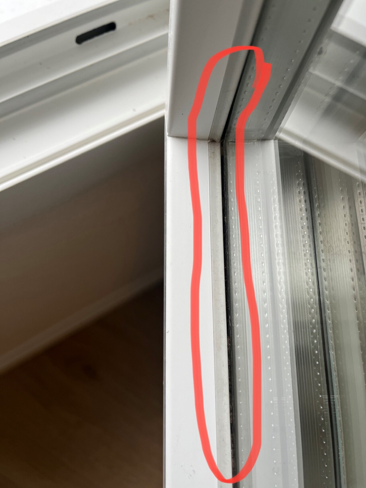 Eine vertikale Lücke in der Fensterabdichtung eines Schiebefensters, rot markiert.