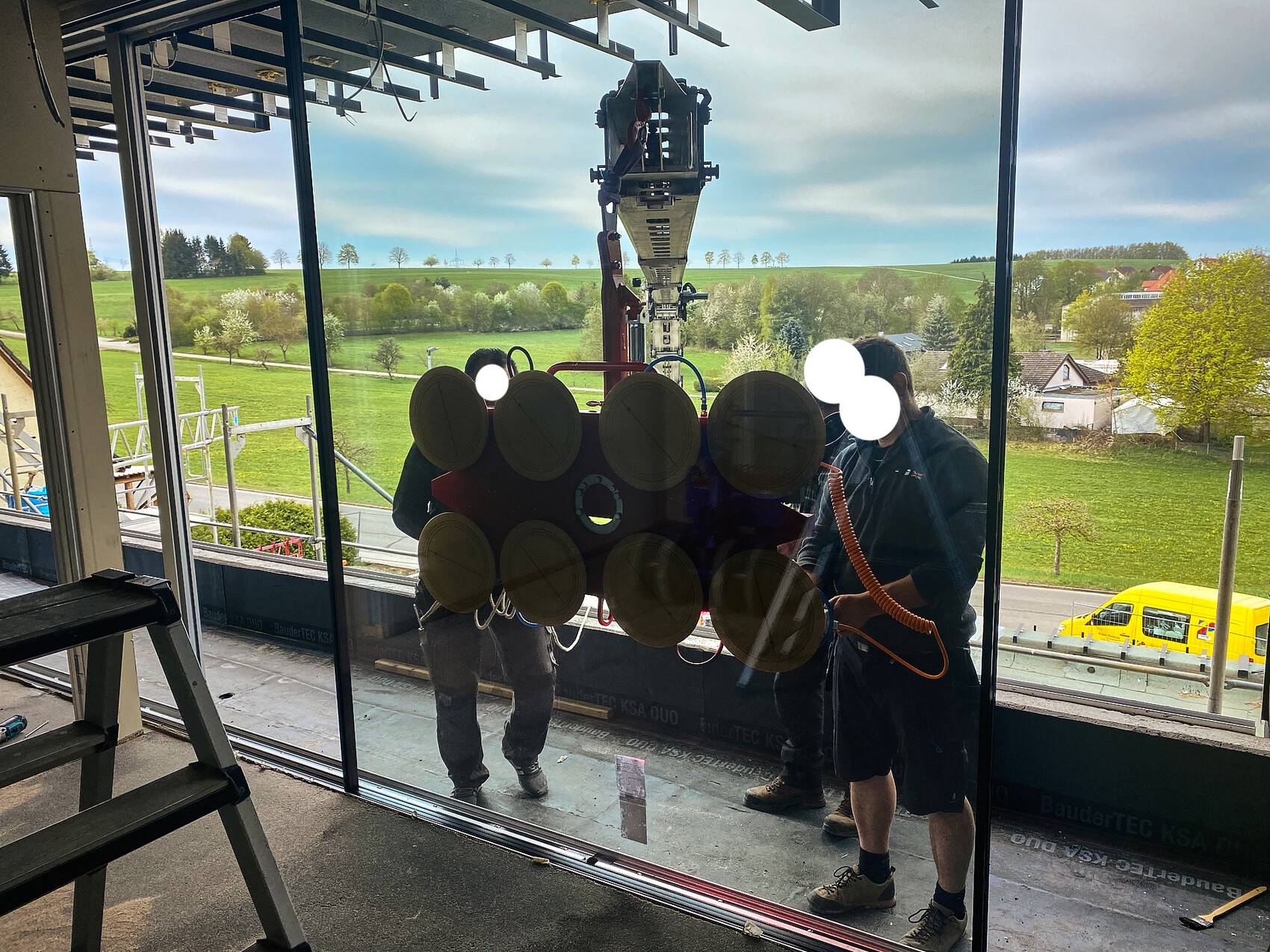 Zwei Arbeiter setzen eine Glasscheibe mit Saugnäpfen in eine Glasfassade ein.