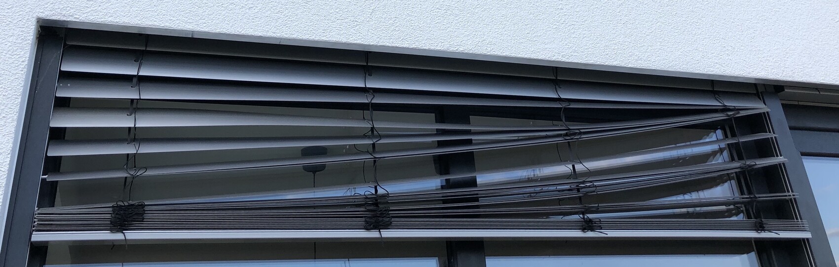 Außenfenster mit horizontalen Jalousien und Zugschnüren, Fensterrahmen sichtbar