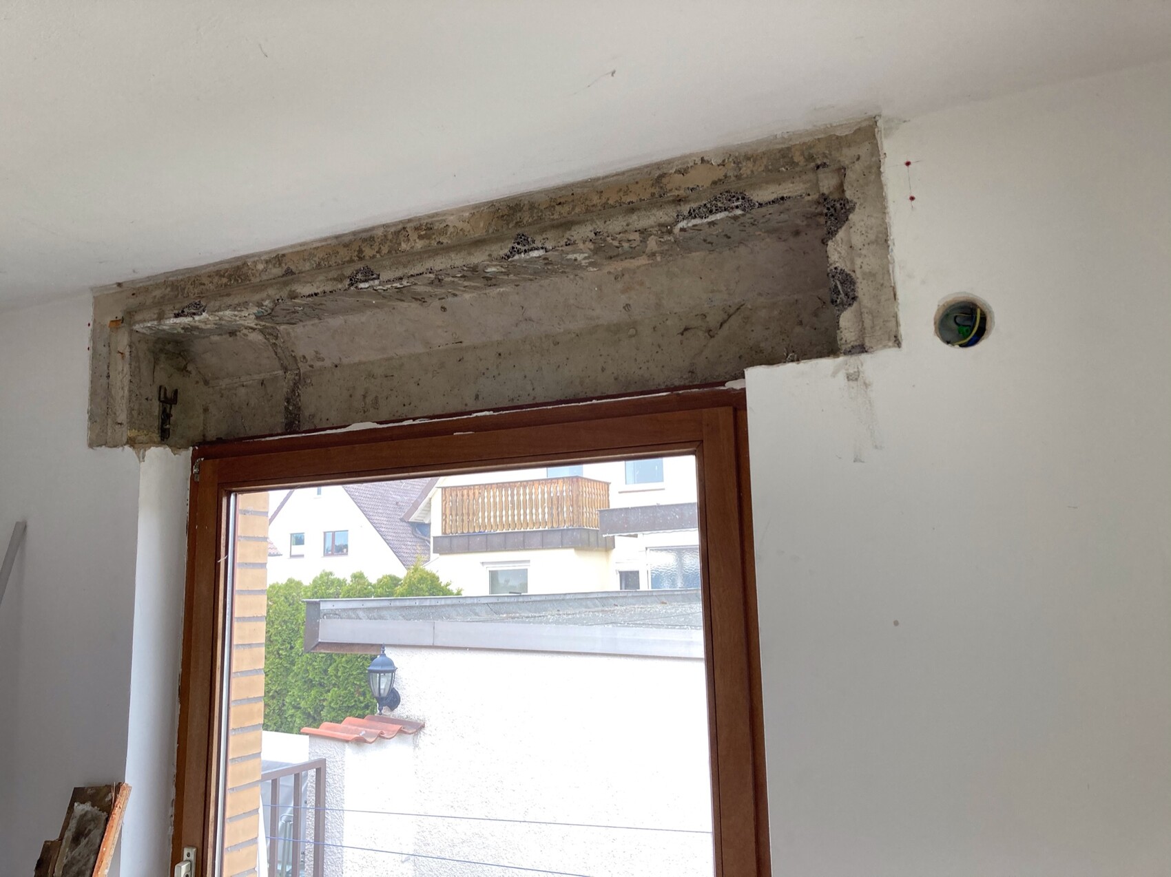 Freigelegter Betonbalken über dem Fensterrahmen; Rohbauwand mit Kabelöffnung sichtbar.