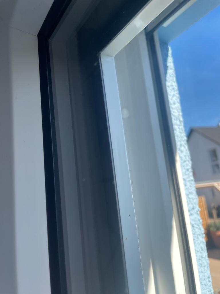 Nahaufnahme eines Fensterrahmens, Blick nach außen auf eine blaue Hausfassade und Dach.