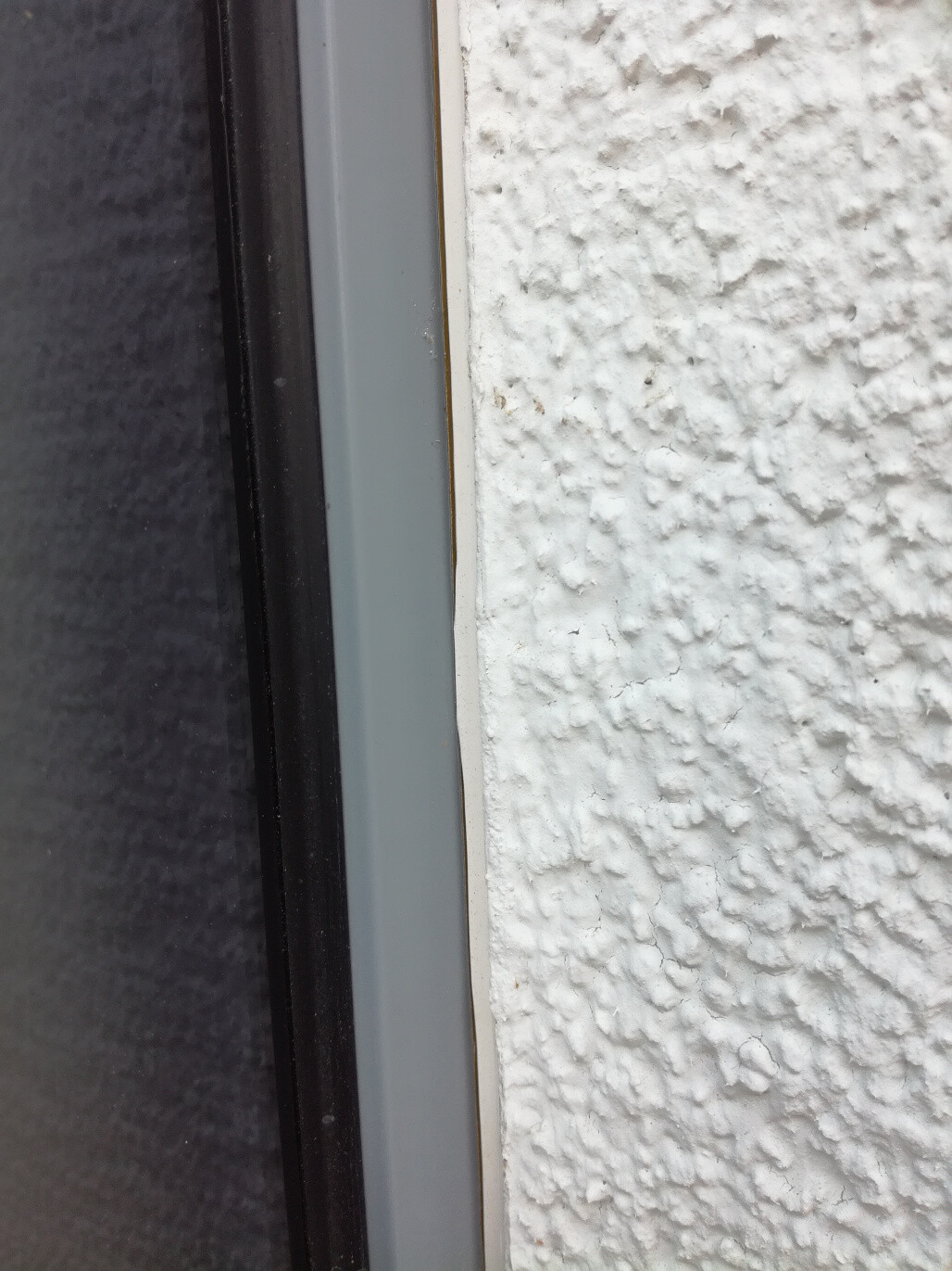 Nahaufnahme Fensterrahmen an weißer grob strukturierter Außenwand.